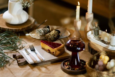 Foto de Una escena cálida mostrando una rebanada de pastel de queso de fresa en una tabla de madera junto a una taza de té de invierno. Ubicado en un mantel de arpillera bajo la luz de las velas ambientales, este ajuste encarna comodidad e indulgencia. - Imagen libre de derechos