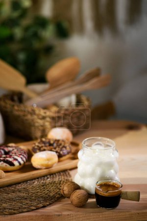 Photo for A wooden platter holds donuts, chocolate-filled cookies, and bite-sized cookies. Behind, walnuts rest on a white cloth, with wooden utensils in a wicker basket. An iced milk with espresso completes the scene - Royalty Free Image