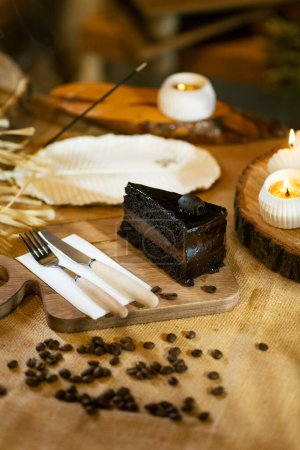 Photo for A slice of chocolate cake elegantly presented with cutlery, candles, and incense, without coffee. Emphasis on atmospheric and rustic aesthetics. - Royalty Free Image