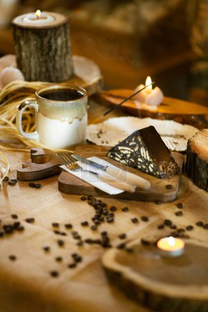 Foto de Pastel de mosaico y café servido en arpillera, con cubiertos de madera y tabla. Mejorado por el incienso y la luz de las velas. - Imagen libre de derechos