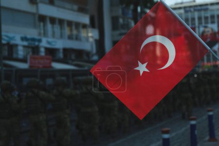 Photo for This striking photograph taken on August 30th, 2023, at Izmir Kordon prominently features a vividly colored Turkish flag in the foreground. In the background, slightly out of focus due to a shallow depth of field, soldiers can be seen marching in a c - Royalty Free Image