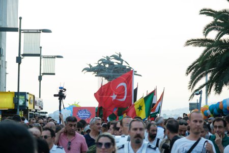 Téléchargez les photos : Izmir, Turquie - 1er septembre 2023 : Des foules agitent des drapeaux de divers pays lors de la marche du cortège d'ouverture de la Foire internationale d'Izmir. La célèbre statue "Cumhuriyet Tree" se dresse en arrière-plan sur la place Cumhuriyet - en image libre de droit