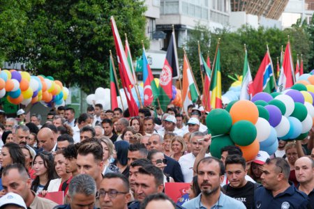 Foto de Izmir, Turquía - 1 de septiembre de 2023: Las multitudes participan alegremente en la marcha de cortejo de apertura de la Feria Internacional de Izmir, ondeando banderas de varias naciones y llevando globos de colores contra un cielo brillante - Imagen libre de derechos
