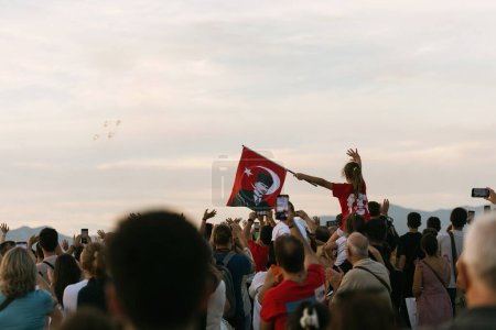 Photo for Izmir, Turkey, September, 9, 2023, in a sea of spectators, a young girl perched on someone's shoulders, proudly waves a Turkish flag bearing Atatrk's image. In the blurred background, the Turkish Stars flight team soars - Royalty Free Image