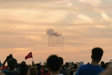 Photo for Izmir, Turkey, September, 9, 2023, amidst the dazzling aerial display by the Turkish Stars, a single Turkish flag, held high and in sharp focus, captures the essence of national pride. The defocused aircrafts in the background, trailing red and white - Royalty Free Image