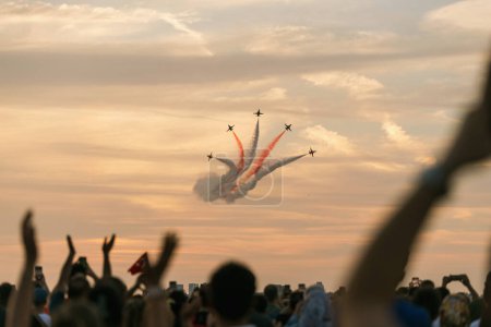 Photo for Izmir, Turkey, September, 9, 2023, on Izmir's Liberation Day, the renowned Turkish Stars aircrafts paint the sky with their breathtaking aerial maneuvers. Leaving trails of red and white smoke behind, they capture the awe of the defocused crowd below - Royalty Free Image