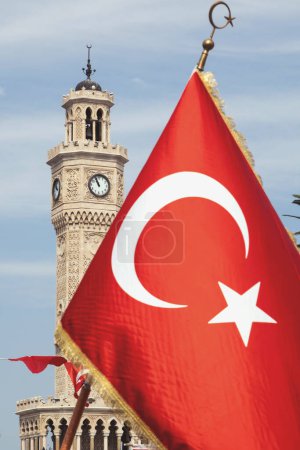 Foto de Izmir, Turquía, 9 de septiembre de 2023: Una fotografía vibrante que muestra una bandera turca ondeando orgullosamente con la famosa Torre del Reloj de Izmir de pie elegantemente al fondo durante las primeras horas - Imagen libre de derechos