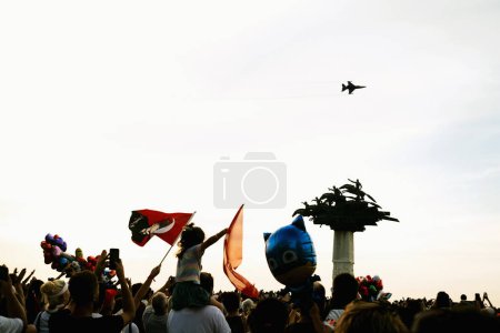Téléchargez les photos : Izmir, Turquie, 9 septembre 2023 : Une mer de gens, agitant des drapeaux turcs sur la place Cumhuriyet, salue l'avion de chasse Solo Turk, avec l'arbre symbolique de la République debout au milieu d'eux - en image libre de droit