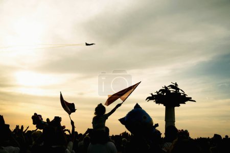 Photo for Izmir, Turkey, September 9, 2023: A sea of people, waving Turkish flags in Cumhuriyet Square, salute the soaring Solo Turk fighter jet, with the symbolic Republic Tree standing tall among them - Royalty Free Image