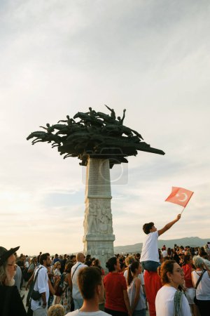 Foto de Izmir, Turquía, 9 de septiembre de 2023: Un niño, posado sobre los hombros de alguien, ondea orgullosamente la bandera turca con el emblemático Monumento al Árbol de la República de pie en el fondo, simbolizando el espíritu y la resiliencia de Izmir. - Imagen libre de derechos