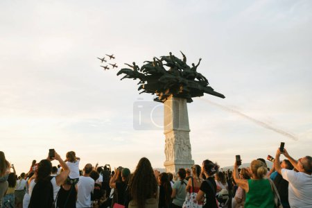 Foto de Izmir, Turquía, 9 de septiembre de 2023: Mientras el sol de la tarde proyecta su luz dorada, las Estrellas Turcas realizan una exhibición aérea. Espectadores cautivados, sosteniendo banderas turcas, se reúnen alrededor del icónico monumento al Árbol Cumhuriyet, conmemorando el aniversario de Izmi - Imagen libre de derechos