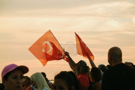 Foto de Izmir, Turquía, 9 de septiembre de 2023, mientras las puestas de sol, cuatro individuos se mantienen unidos, ondeando la bandera turca contra el telón de fondo de un vibrante cielo al atardecer, simbolizando la unidad y el orgullo durante las celebraciones del Día de la Liberación. - Imagen libre de derechos