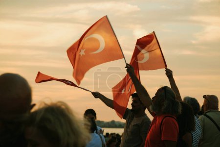 Téléchargez les photos : Izmir, Turquie, le 9 septembre 2023, alors que les couchers de soleil se couchent, quatre individus se tiennent unis, agitant le drapeau turc sur fond de ciel couchant vibrant, symbolisant l'unité et la fierté lors des célébrations du Jour de la Libération. - en image libre de droit