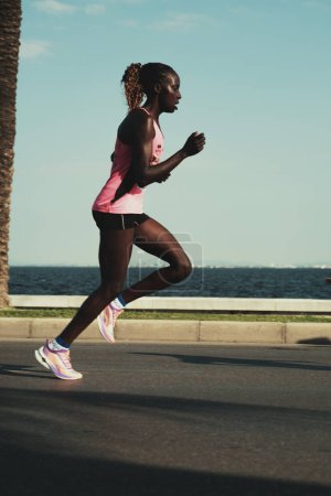 Photo for Izmir, Turkey, September 10, 2023: An African Black woman, dressed in pink running shoes and attire, strides along the seafront at Goztepe in the Half Marathon - Royalty Free Image