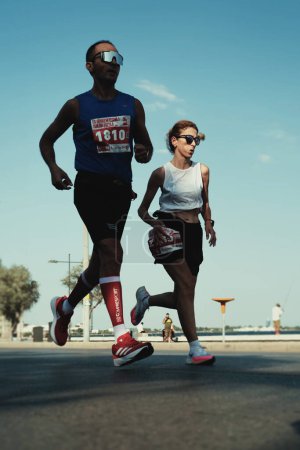 Téléchargez les photos : Izmir, Turquie, 10 septembre 2023 : Un homme à Nike et une femme à Adidas courent côte à côte le long de la mer de Goztepe, symbolisant l'unité dans le demi-marathon d'Izmir - en image libre de droit