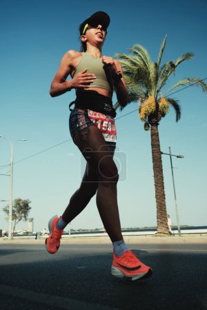 Téléchargez les photos : Izmir, Turquie, 10 septembre 2023 : Une femme en chaussures Nike orange court le long de la mer de Goztepe, avec une toile de fond de palmier, dans le demi-marathon d'Izmir - en image libre de droit