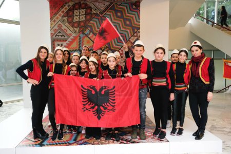 Photo for Tirana, Albania - November 28, 2023: Students and teachers in traditional Albanian costumes pose with the flag in front of a traditional backdrop at the Palace of Congresses - Royalty Free Image