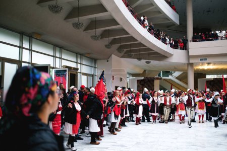 Foto de Tirana, Albania - 28 de noviembre: La gente con atuendo tradicional albanés baila en círculo durante las celebraciones del Día de la Independencia, rodeada de banderas - Imagen libre de derechos
