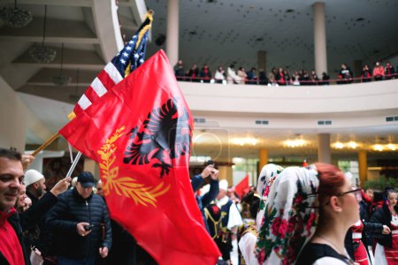 Foto de Tirana, Albania - 28 de noviembre: Gente con atuendo tradicional bailando en círculo con banderas albanesas y americanas durante las celebraciones en el Palacio - Imagen libre de derechos