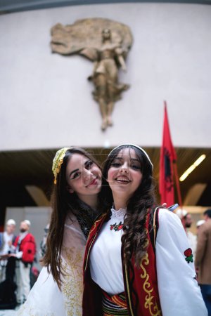 Foto de Tirana, Albania - 28 de noviembre: Dos alumnas con atuendo tradicional albanés posan frente a la estatua de la Madre Teresa en el Palacio - Imagen libre de derechos
