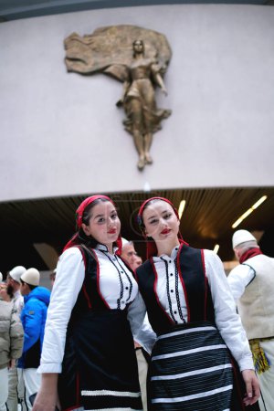 Foto de Tirana, Albania - 28 de noviembre: Dos alumnas con atuendo tradicional albanés posan frente a la estatua de la Madre Teresa en el Palacio - Imagen libre de derechos