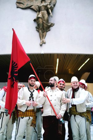 Photo for Tirana, Albania - November 28, Albania's Independence Day Men in traditional Albanian dress pose with flags at the Palace of Congresses, Mother Teresa statue in the background. - Royalty Free Image