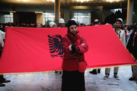 Foto de Tirana, Albania - 28 de noviembre: Una mujer albanesa posa frente a una gran bandera nacional durante las celebraciones del Día de la Independencia en el Palacio de Congresos de Nene Tereza - Imagen libre de derechos