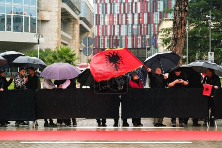 Photo for Tirana, Albania - November 28, 2023: On a rainy Independence Day, citizens with Albanian flags and umbrellas watch the parade from the roadside at avenue of martyrs of the nation Boulevard avenue of martyrs of the nation - Royalty Free Image