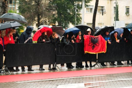 Photo for Tirana, Albania - November 28, 2023: On a rainy Independence Day, citizens with Albanian flags and umbrellas watch the parade from the roadside at avenue of martyrs of the nation Boulevard avenue of martyrs of the nation - Royalty Free Image