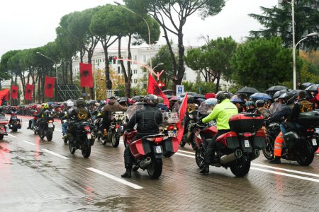 Téléchargez les photos : Tirana, Albanie - 28 novembre 2023 : Sur l'avenue des martyrs de la nation lors d'un jour pluvieux de l'indépendance, un groupe de motards défilant avec des drapeaux albanais tandis que le public regarde avec des drapeaux et des parapluies - en image libre de droit