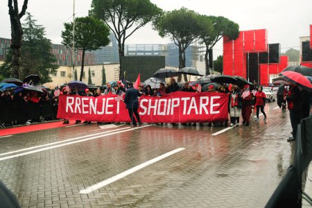 Photo for Tirana, Albania - November 28, 2023: On Avenue of Martyrs of the Nation, in front of Mother Teresa Palace, participants with a Prenjet Shqiptare banner march with American and Albanian flags on a rainy Independence Day - Royalty Free Image