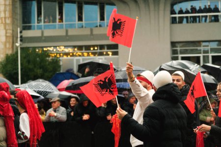 Téléchargez les photos : Tirana, Albanie - 28 novembre 2023 : Sur l'avenue des martyrs de la nation, près du palais Mère Teresa, les étudiants en tenue traditionnelle défilent avec des drapeaux albanais à la main le jour de l'indépendance pluvieux, tandis que les spectateurs avec des parapluies et des drapeaux regardent dans la ba - en image libre de droit