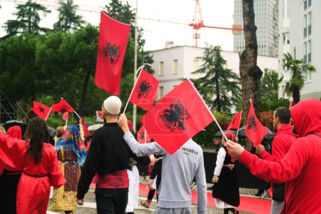 Téléchargez les photos : Tirana, Albanie - 28 novembre 2023 : Sur l'avenue des martyrs de la nation, étudiants et personnes en tenue traditionnelle défilent avec enthousiasme avec des drapeaux albanais le jour de l'indépendance pluvieux, avec des spectateurs tenant des parapluies et des drapeaux en arrière-plan. - en image libre de droit