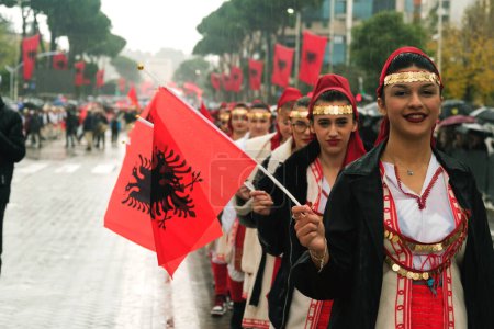 Photo for Tirana, Albania - November 28, 2023: On Avenue of Martyrs of the Nation, during a rainy Independence Day, girl students march in line, smiling and holding Albanian flags with enthusiasm. - Royalty Free Image