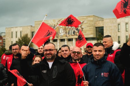 Foto de Tirana, Albania - 28 de noviembre de 2023: En la plaza Skanderbeg, en un lluvioso Día de la Independencia, vemos a la multitud participando con entusiasmo en las celebraciones, sosteniendo banderas albanesas, con el Museo Nacional de Historia de Tirana en el fondo. - Imagen libre de derechos