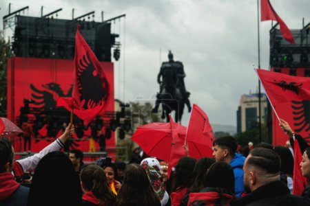 Photo for Tirana, Albania - November 28, 2023: On a rainy Independence Day at Skanderbeg Square, a photo captures the stage near the Skanderbeg statue, adorned with two Albanian flags, and the crowd holding Albanian flags to celebrate the occasion. - Royalty Free Image