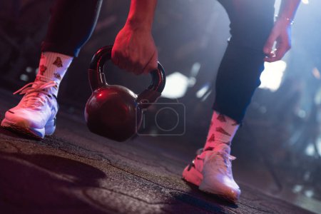 Téléchargez les photos : L'essence lunatique d'une séance de gym capturée dans les pieds d'un athlète prêt à soulever une kettlebell noire - en image libre de droit