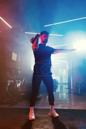 Téléchargez les photos : Un homme effectue une prise de kettlebell dans une salle de gym, avec un éclairage artistique bleu et rouge et une atmosphère subtilement brumeuse - en image libre de droit