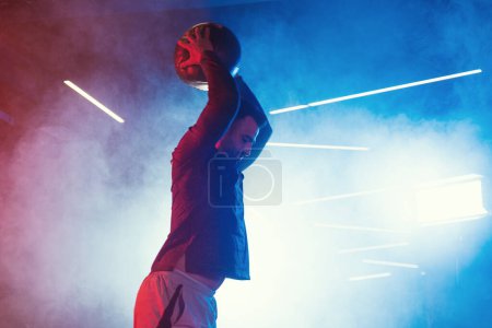 Téléchargez les photos : Un moment d'entraînement intense comme un athlète masculin claque une boule de médecine au sol, entouré d'une lueur brumeuse de lumières rouges et bleues - en image libre de droit