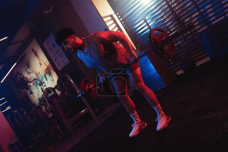 Photo for A male athlete is captured doing barbell rows in a gym, surrounded by the dramatic interplay of blue and red lighting and a light mist - Royalty Free Image