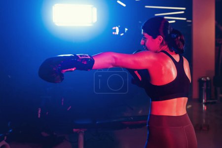 Foto de Una atleta comprometida practica sus golpes bajo dramáticas luces azules y rojas, en un ambiente de gimnasio lleno de niebla - Imagen libre de derechos