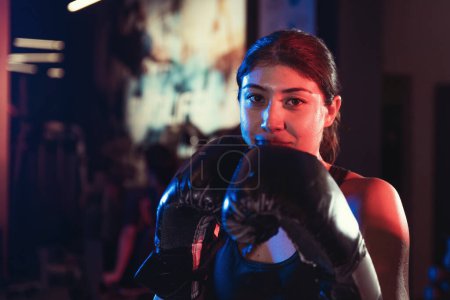 Photo for A committed female athlete practices her punches under dramatic blue and red lights, in a mist-filled gym setting - Royalty Free Image