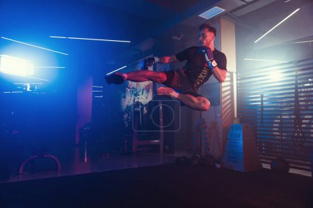 Téléchargez les photos : Une puissante performance de kickboxing sous des lumières brumeuses et colorées dans la salle de gym - en image libre de droit