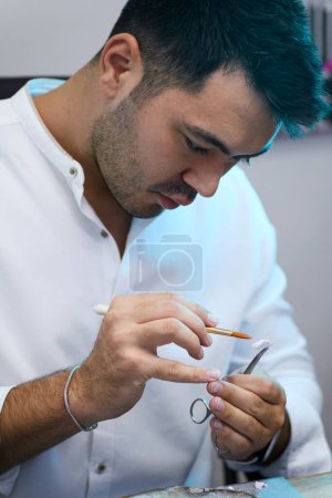 Téléchargez les photos : Gros plan des mains d'un technicien qui applique méticuleusement une dentine en porcelaine sur une prothèse dentaire, à l'aide d'un pinceau pour un travail minutieux, dans un laboratoire dentaire - en image libre de droit