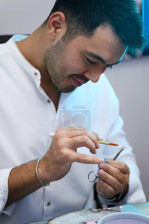 Téléchargez les photos : Gros plan des mains d'un technicien qui applique méticuleusement une dentine en porcelaine sur une prothèse dentaire, à l'aide d'un pinceau pour un travail minutieux, dans un laboratoire dentaire - en image libre de droit