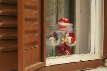 Photo for A festive Santa Claus toy stands guard at a home's window, its cheerful demeanor juxtaposed against the worn frame - Royalty Free Image