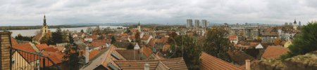 Foto de Belgrado, Serbia - 2 de diciembre de 2023: Una vista panorámica desde la Torre Zemun muestra la fusión de iglesias históricas y estructuras industriales a lo largo del serpenteante Danubio, bajo una nube esparcida por el cielo - Imagen libre de derechos