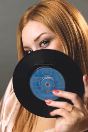 Téléchargez les photos : Une jeune femme regarde à travers le centre d'un disque vinyle, fusionnant mode et nostalgie de la musique. - en image libre de droit