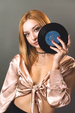 A young woman gazes through the center of a vinyl record, merging fashion with music nostalgia.