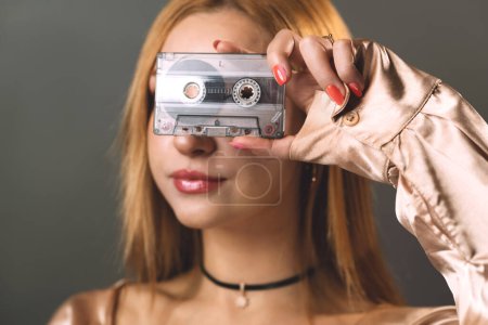 Foto de Una mujer joven oscurece creativamente sus ojos con una cinta de cassette de música vintage. - Imagen libre de derechos